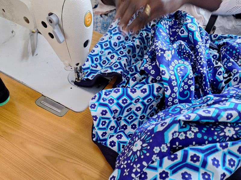 Hands at a sewing machine joining a blue kanga print to its navy fleece backing
