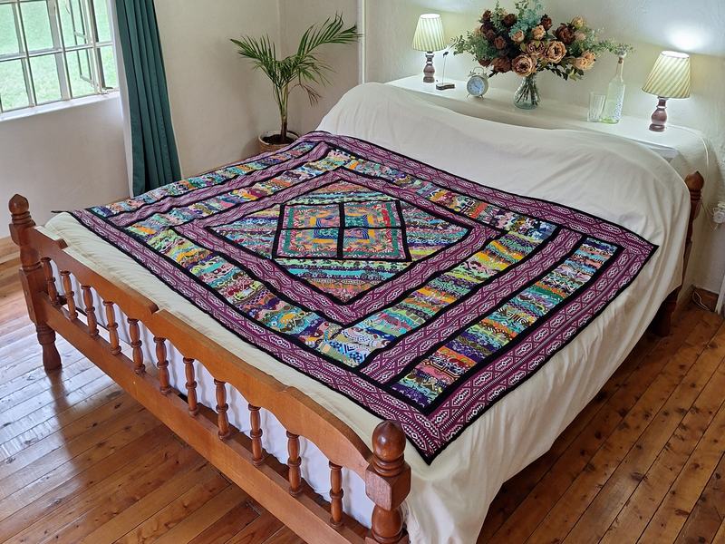 A kanga patchwork quilt in purples and pinks laid on a double bed in a guest room