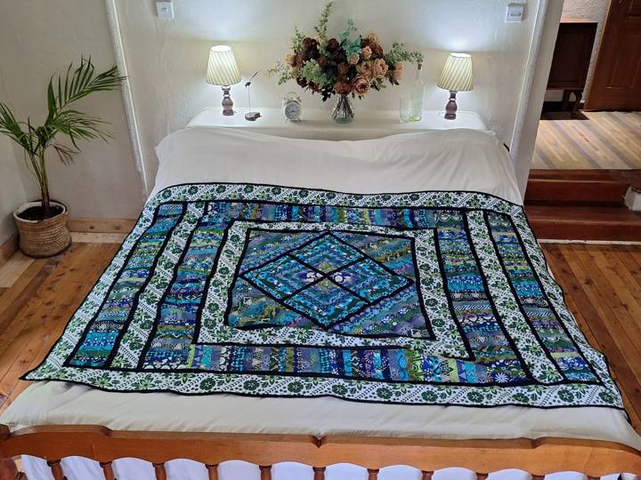A kanga patchwork quilt laid across a double bed in a guest room