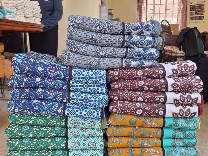 Finished gift sets of kanga bags and fleece blankets stacked in matching blues, teals and ochres