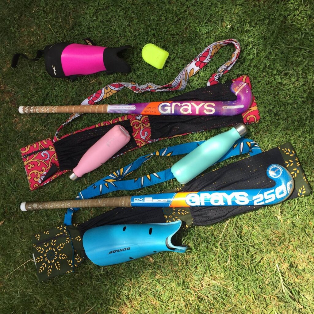 Hockey sticks in kanga stick bags laid on grass with water bottles and shin guards