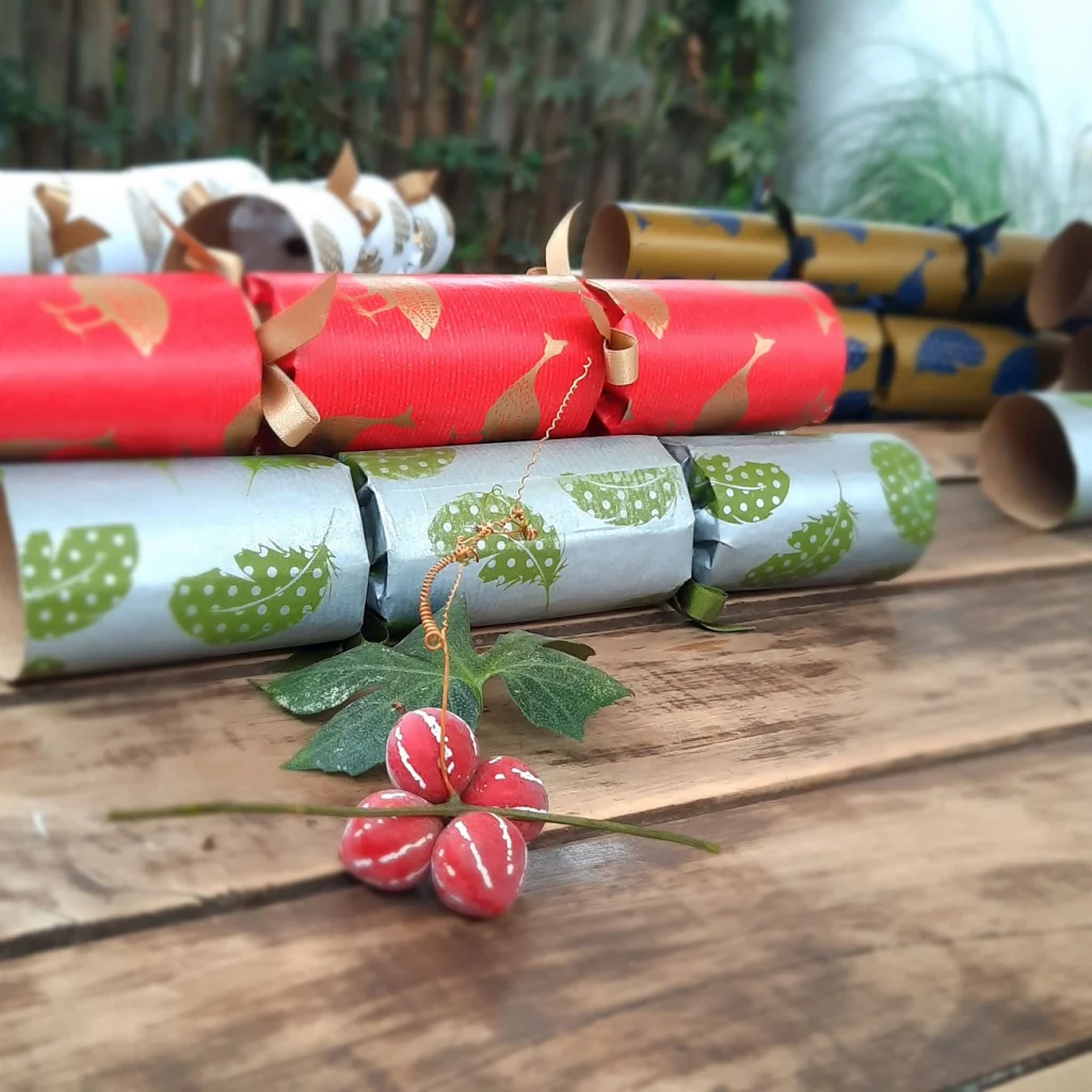 Christmas crackers in red, silver and gold with guinea fowl and feather prints on a wooden table