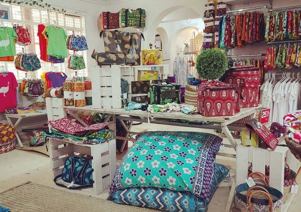 A shop display of kanga cooler bags, floor cushions, baskets and clothing on white wooden crates