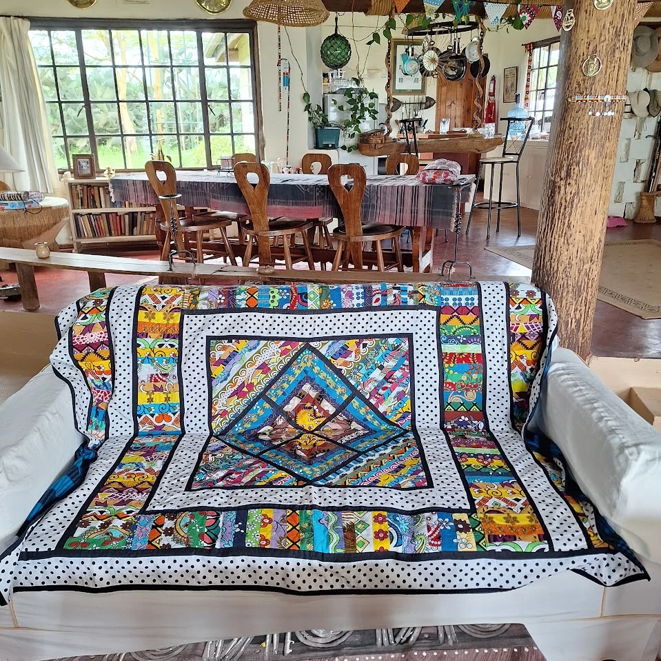 A kanga patchwork quilt with polka-dot borders draped over a white sofa in a sitting room