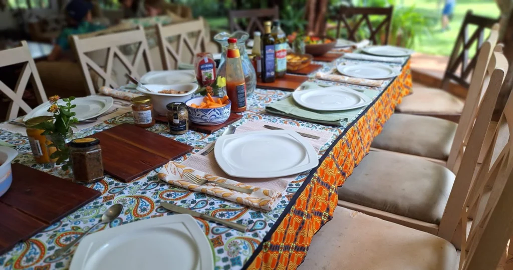 A long table laid with a paisley tablecloth with an orange print border, matching napkins and white plates